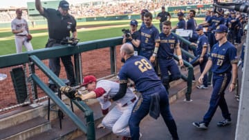 Jun 19, 2022; Omaha, NE, USA; Oklahoma Sooners first baseman Blake Robertson (26) is helped up by Notre Dame Fighting Irish pitcher John Michael Bertrand (28) after falling into the dugout during the first inning at Charles Schwab Field. Mandatory Credit: Dylan Widger-USA TODAY Sports